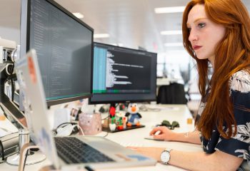 Woman focused on coding with laptop and two screens